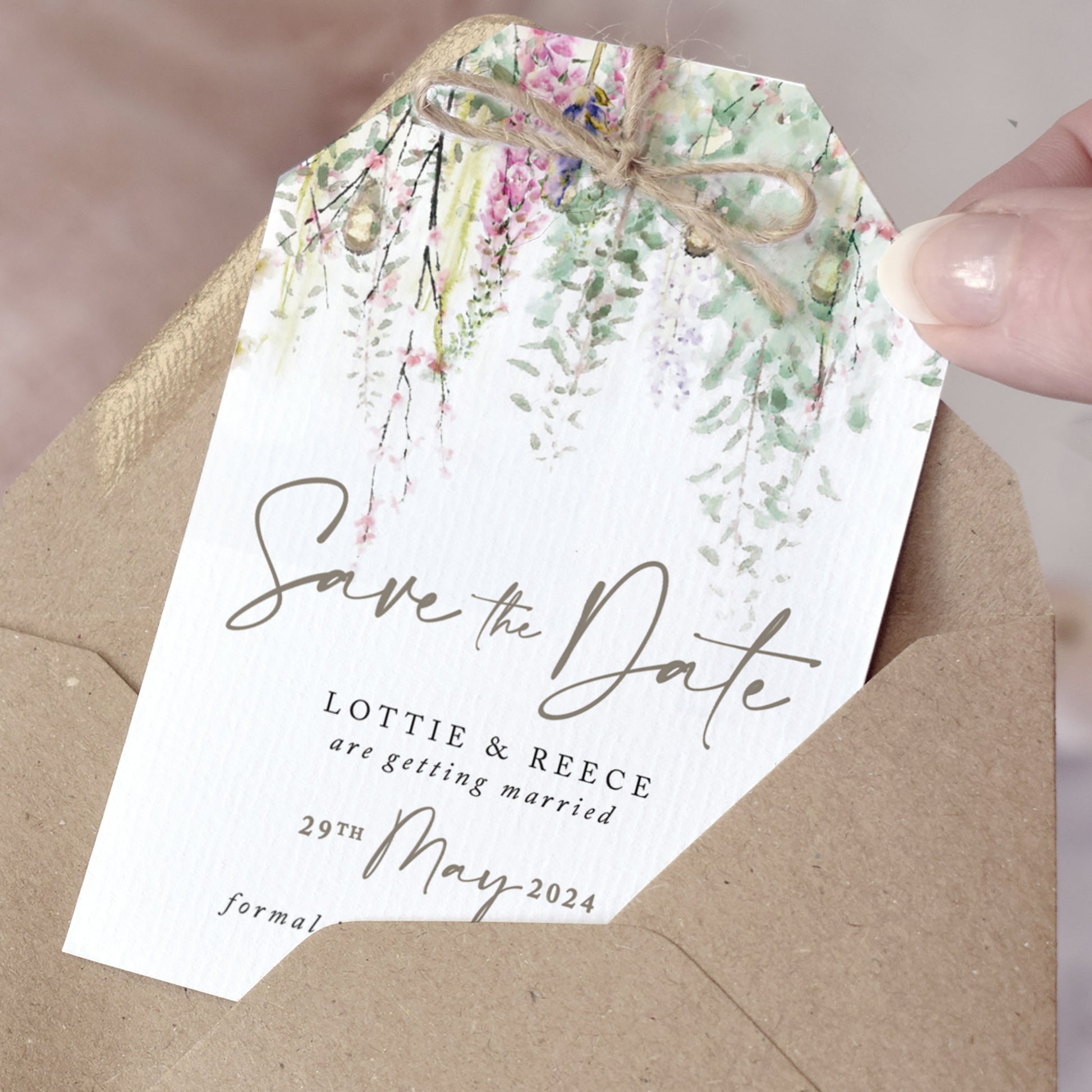 Rustic Save the Date cards cut into a tag shape and finished with a jute twine bow. The design features sage green foliage with whimsical flowrers and string lights. The typography is simple and modern with caligraphy style accents.